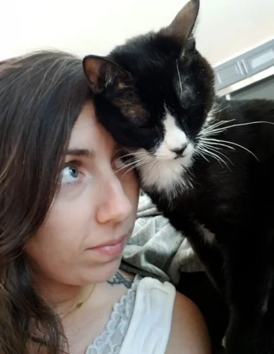 A woman looks affectionately at a black and white cat resting its head against hers, sharing a quiet and close moment.